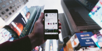 Close up of a person holding their phone in front of tall buildings and a gray sky.