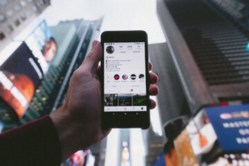 Close up of a person holding their phone in front of tall buildings and a gray sky.