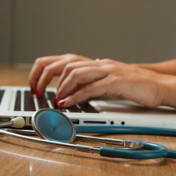 person typing on laptop next to a stethoscope