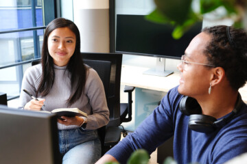 Two people talking, one taking notes, the other showing something on a computer.