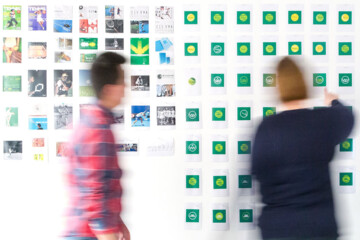 Two people looking at books and brand logos hanging on a white wall.