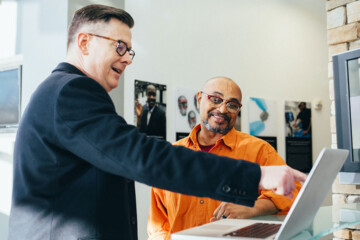 Two men in an office review SEO performance on a laptop.