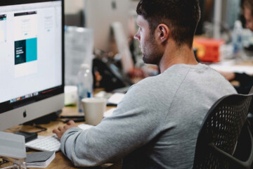 A man designing a website on an iMac at his desk.