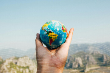 A hand holding a small globe in front of mountain scenery.