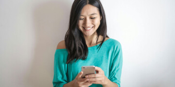 Woman in a green shirt smiling as she looks at her smartphone.