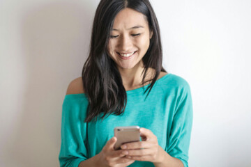 Woman in a green shirt smiling as she looks at her smartphone.