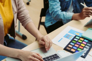 Two female coworkers working at a shared desk with laptops.